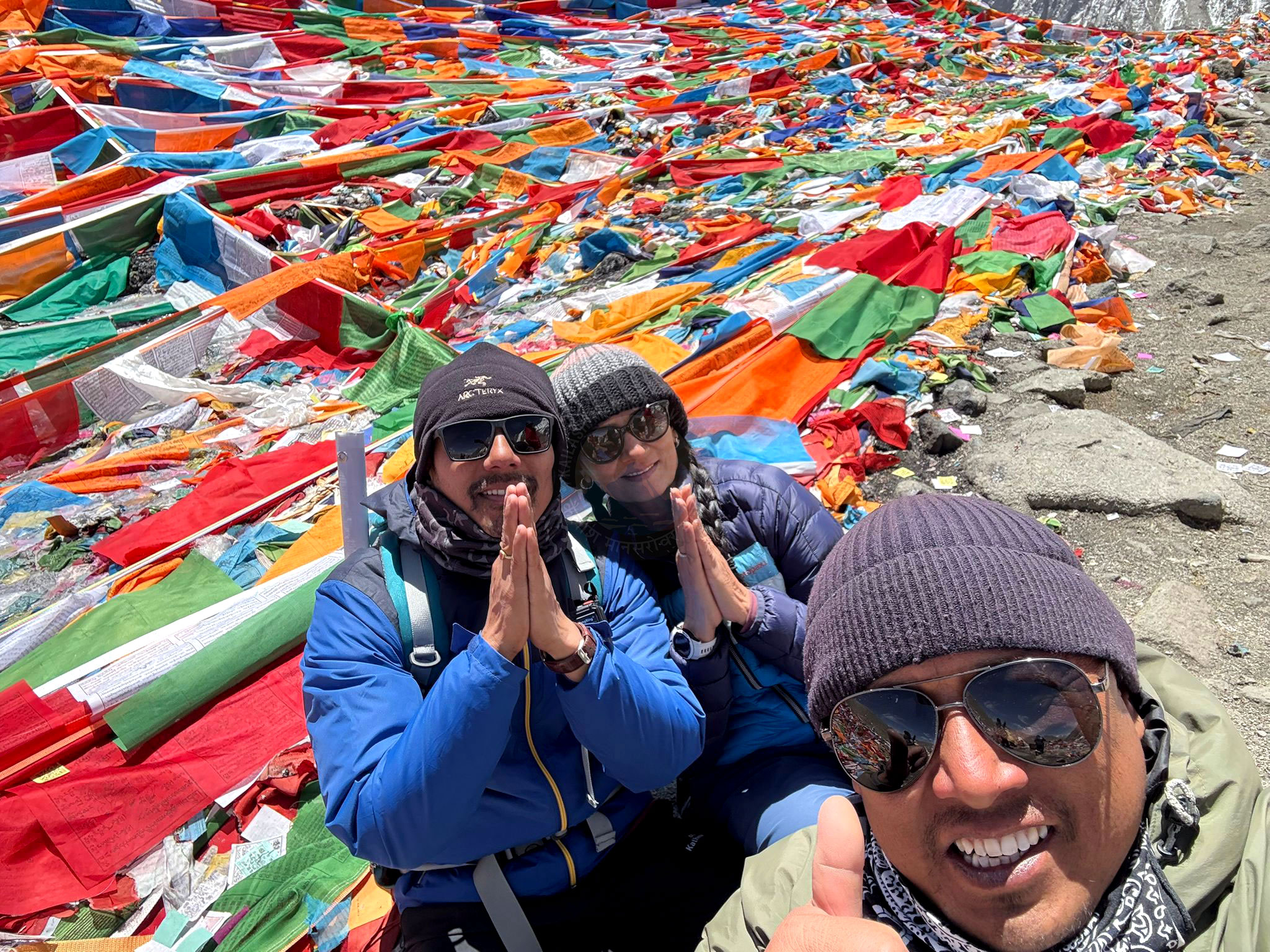 Pilgrims surrounded by vibrant rainbow prayer flags during Kailash Yatra, engaging in spiritual traditions