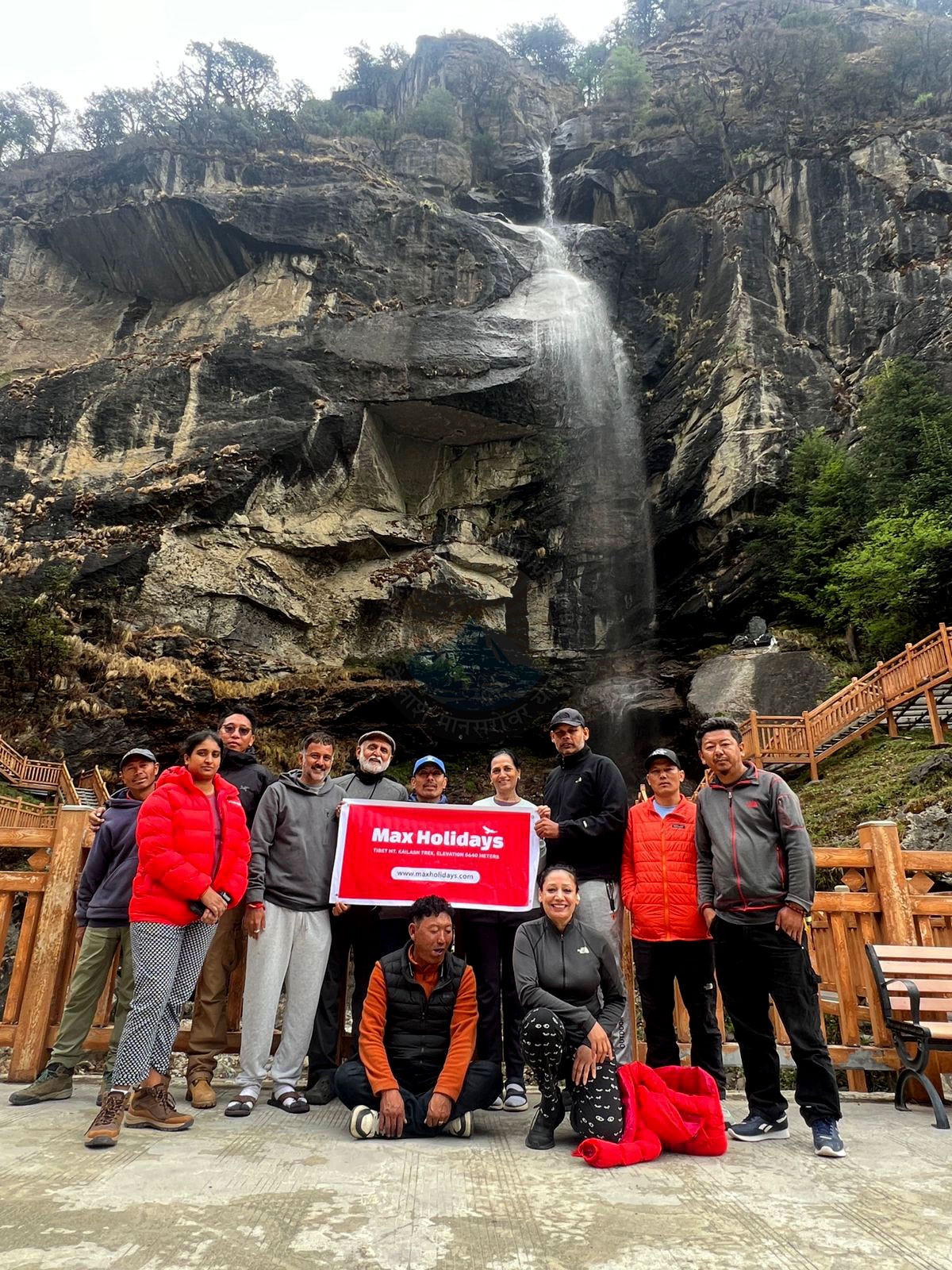 Group of yatris smiling together in front of Bhimdhara Waterfall during Kailash pilgrimage, experiencing joy and camaraderie