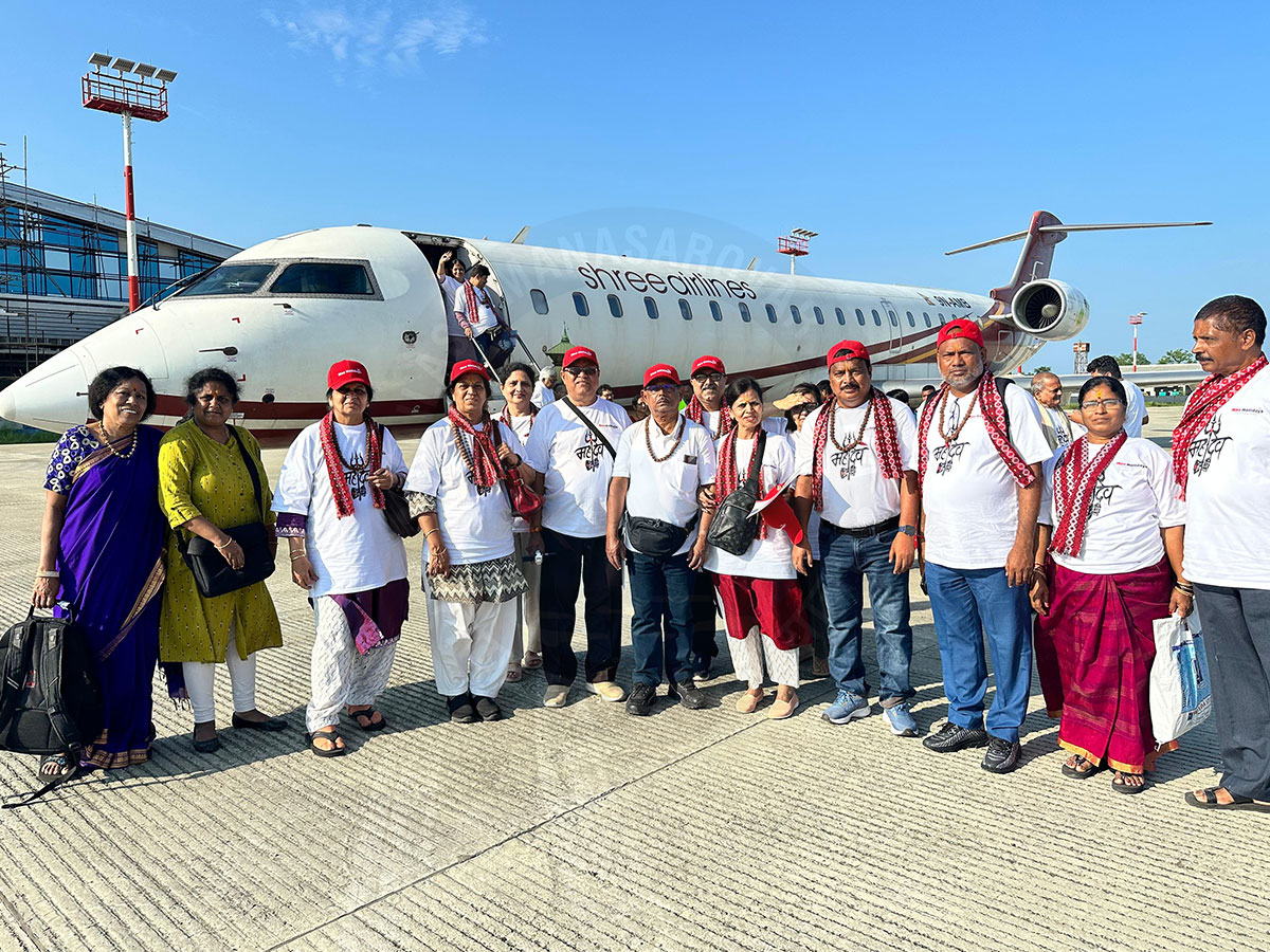Group of Indian pilgrims posing in front of Shree Airlines aircraft on the airport tarmac before boarding