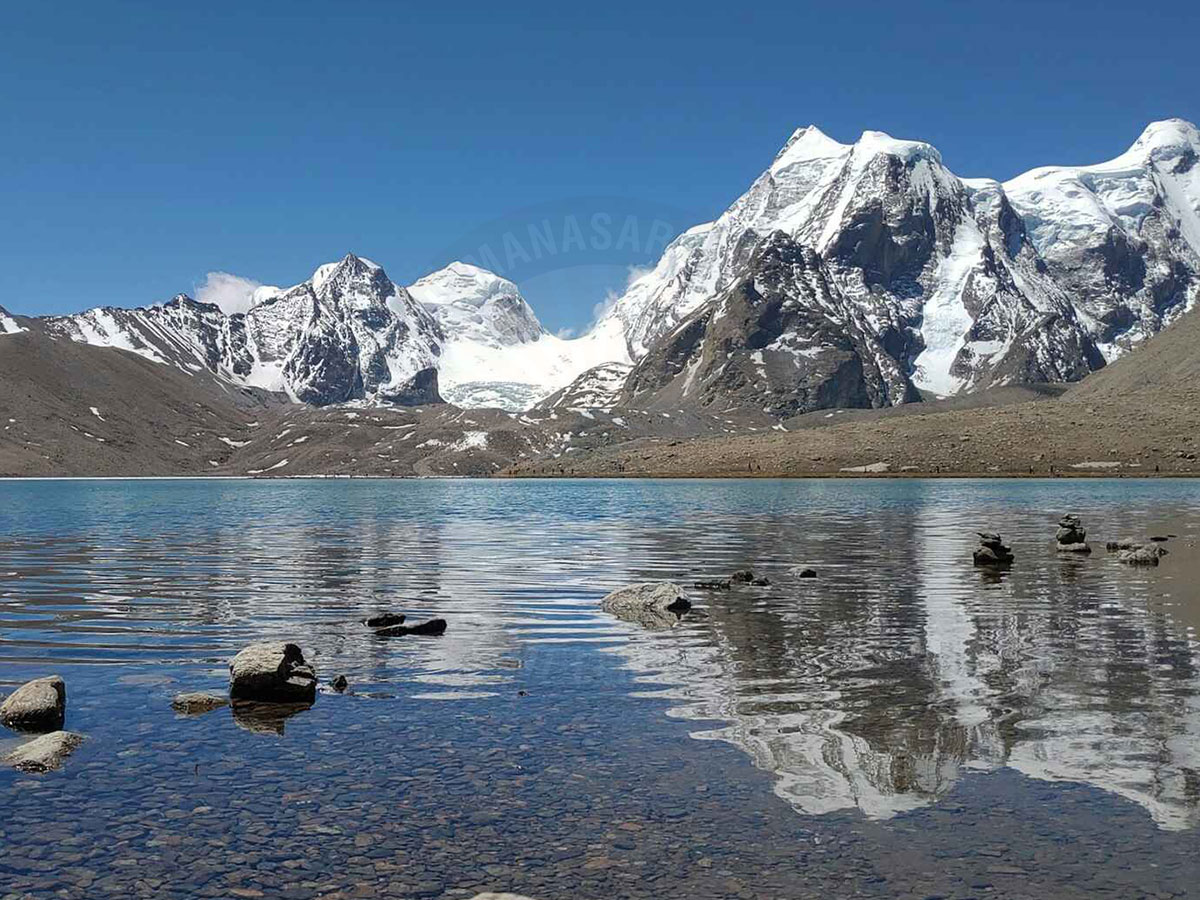 Scenic view of Gurudongmar Lake in Sikkim surrounded by snow-capped Himalayan mountains under a clear blue sky