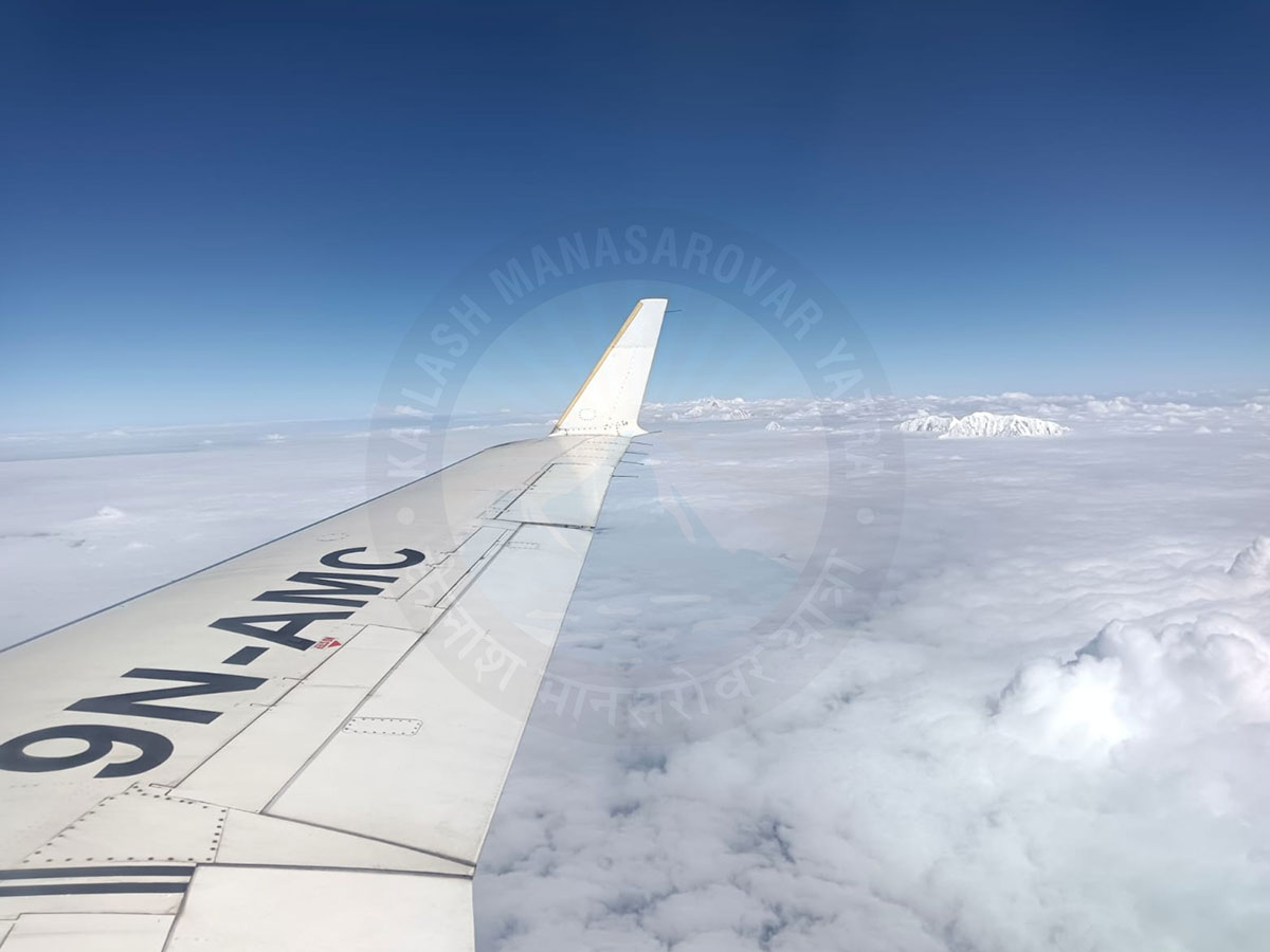 View from airplane window showing Himalayan mountain peaks and clouds during Kailash Manasarovar Yatra