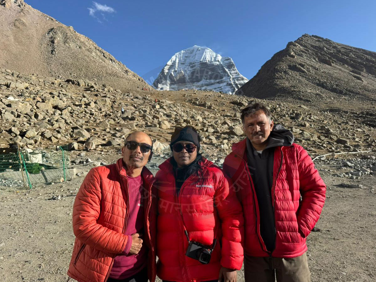 Devotees in red jackets posing during Kailash Mansarovar Yatra with sacred Mount Kailash in the background