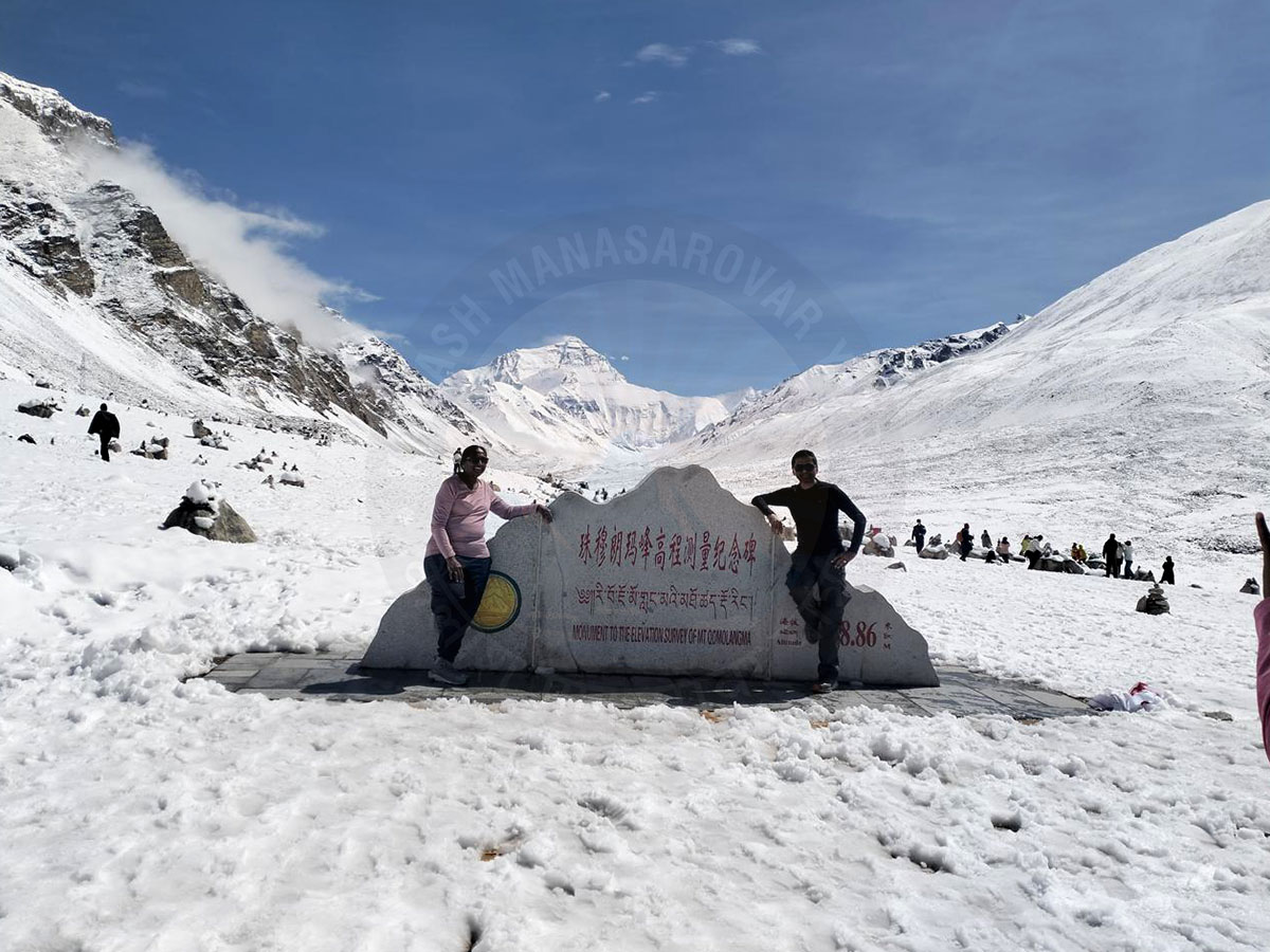 Tourists posing at the stone monument near Mount Everest Base Camp North in Tibet, with the snow-covered Himalayan mountains in the background.