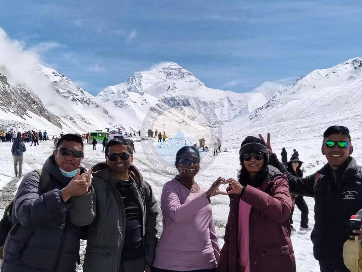 Group of happy travelers posing at Mount Everest Base Camp with the majestic snow-covered peak of Mount Everest in the background.